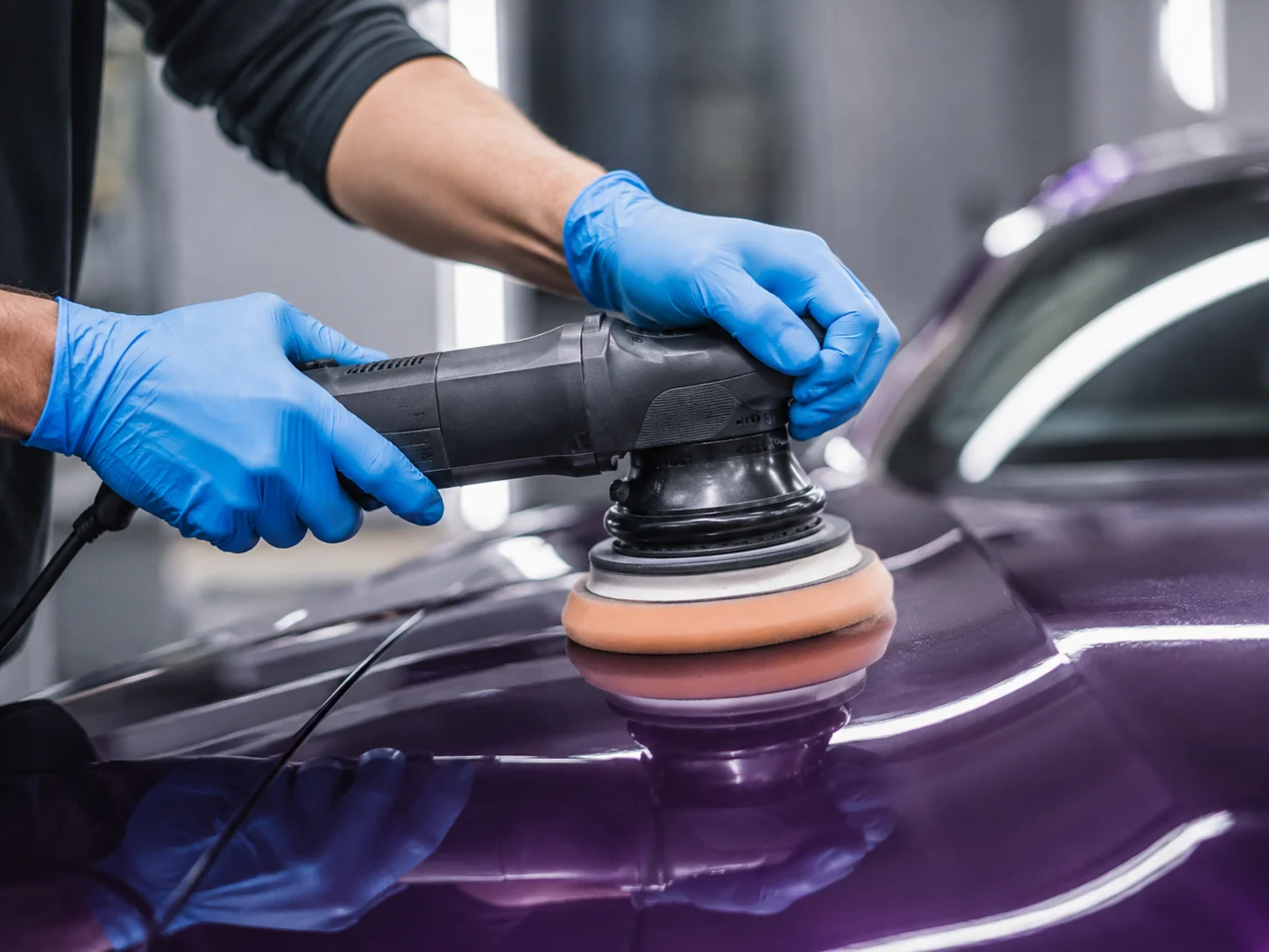 Мастер в защитных перчатках полирует фиолетовый кузов автомобиля